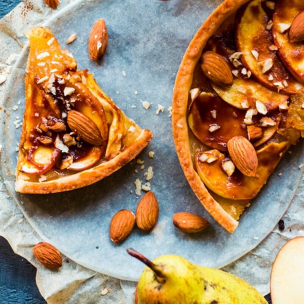 Apfel-Karamell-Kuchen wird mit Mandeln bestreut und angeschnitten serviert