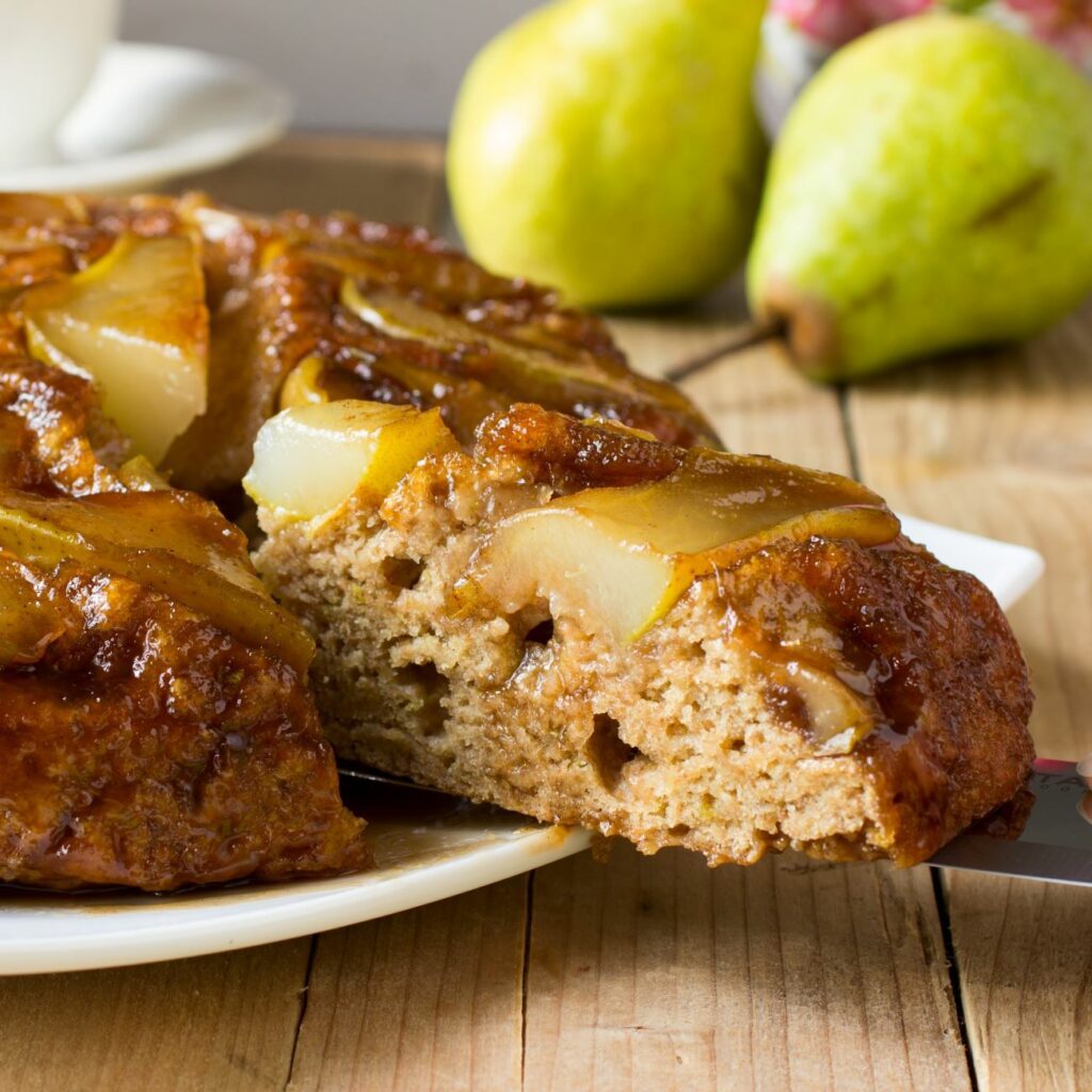 Veganer Birnenkuchen wird angeschnitten und ein Stück wird auf einem Tortenheber herausgezogen