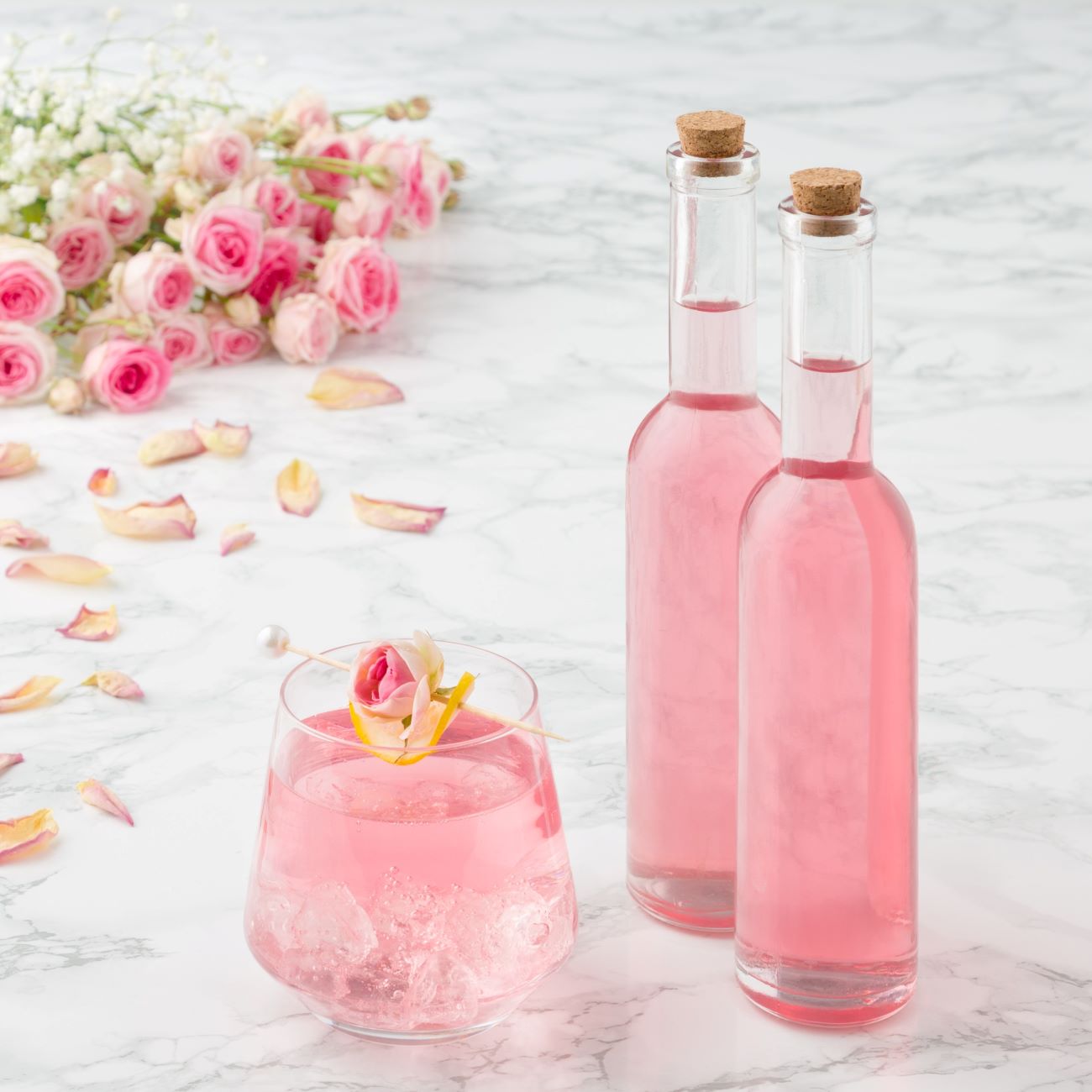 Růžový sirup se podává ve dvou malých lahvičkách a sklenici s kostkami ledu.