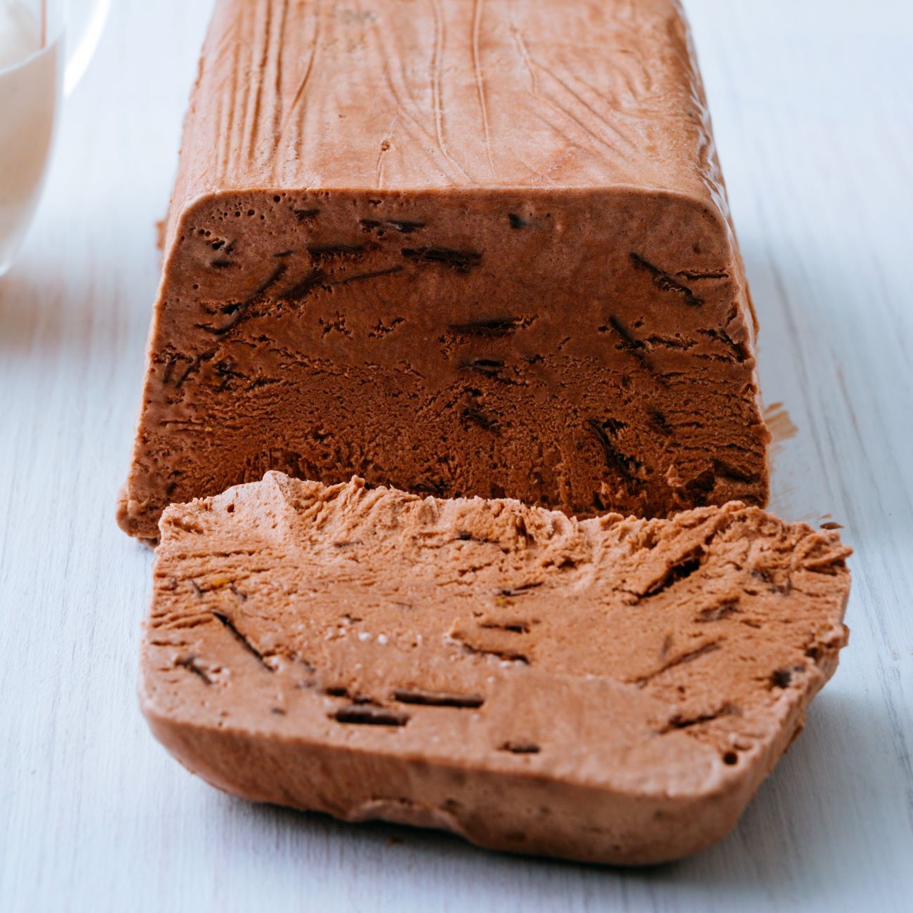 Čokoládový parfait je zobrazen nakrájený na bílé dřevěné desce.