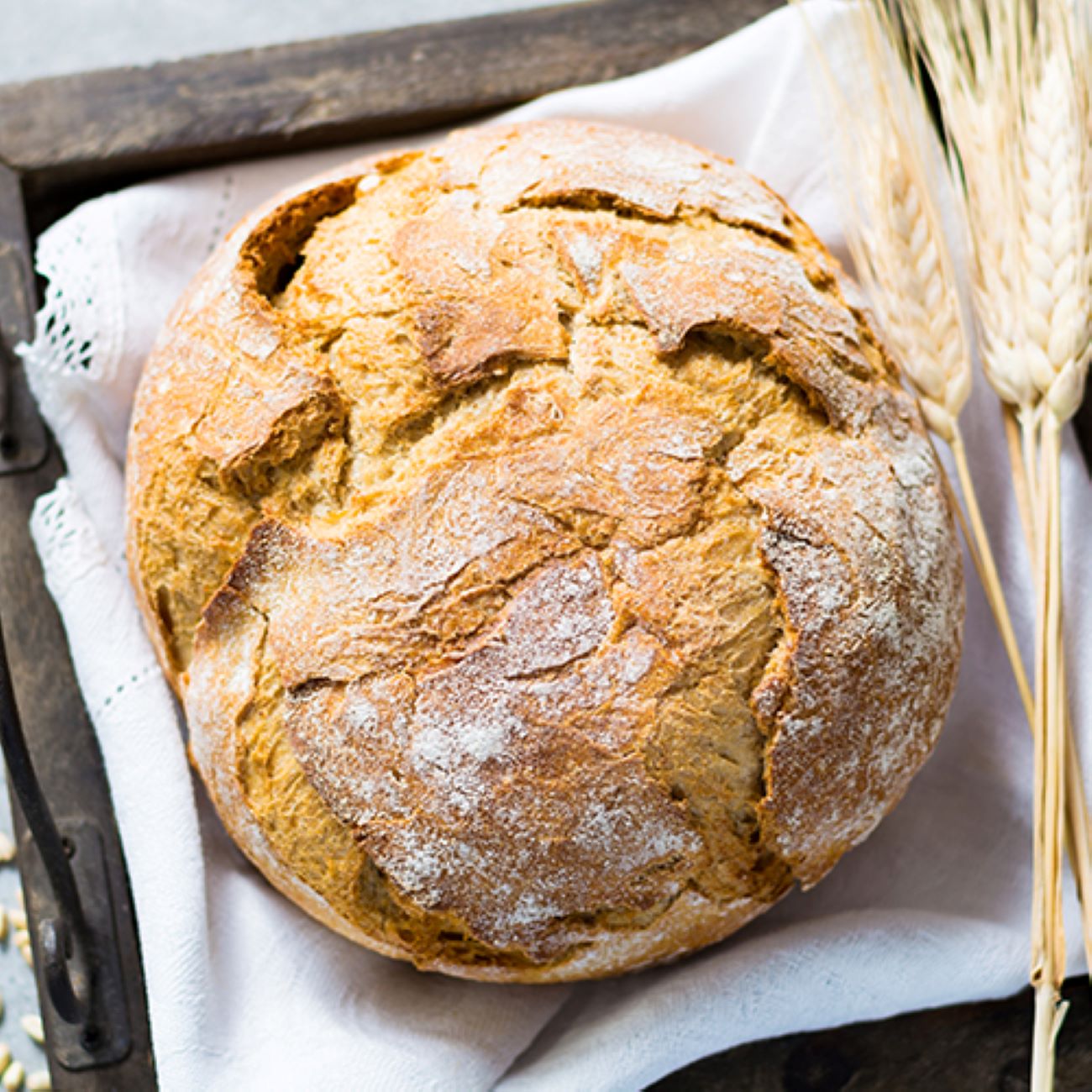 Pšeničný chléb je zobrazen shora na bílém plátně a zdoben pšenicí.
