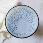 Blaue Mandelmilch wird von oben in einem Glas auf einem grauen Untergrund gezeigt.