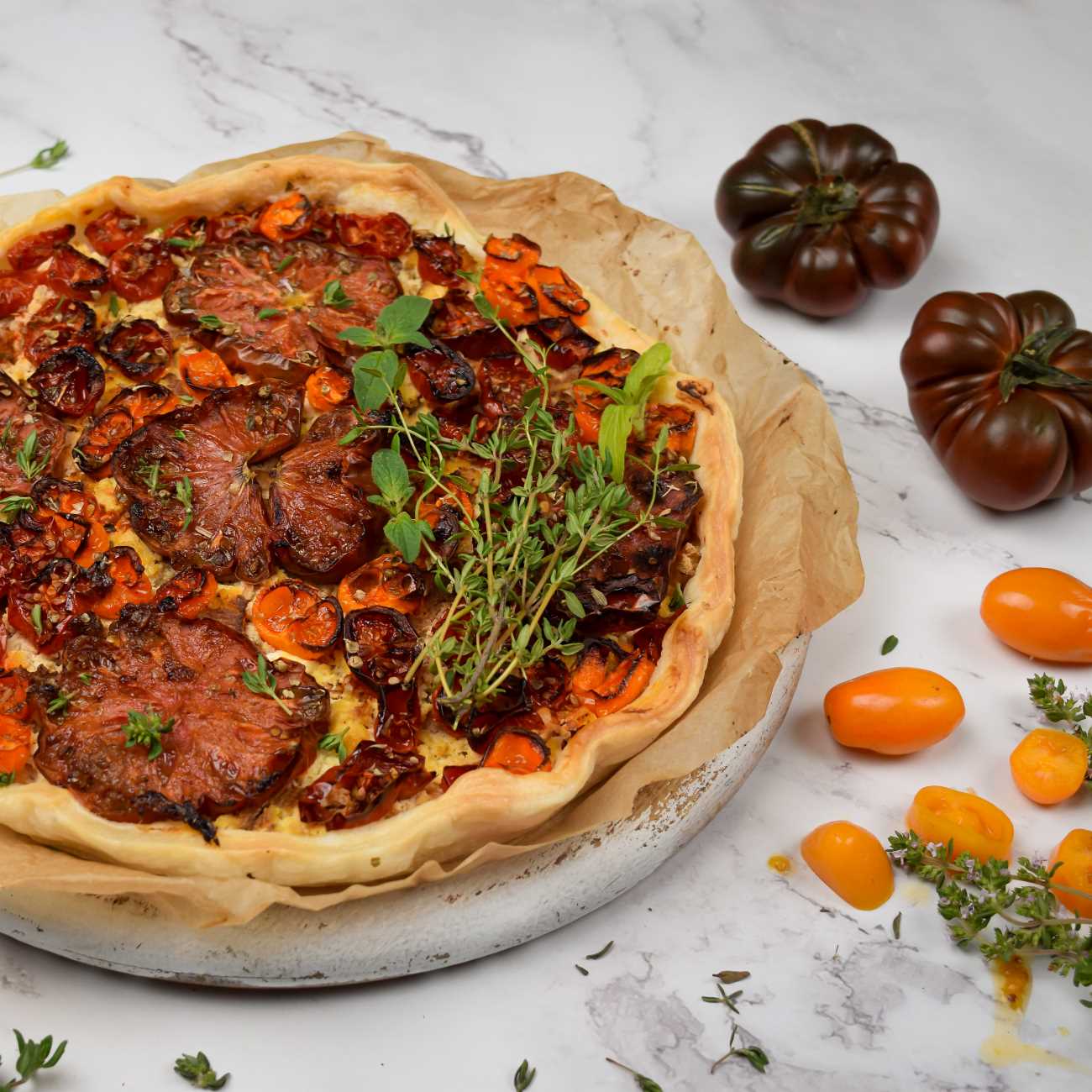 Tomaten Quiche wird mit Backpapier auf einem Brett gezeigt.