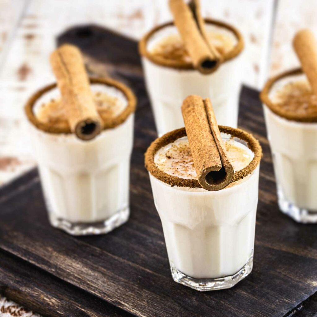 Eierlikör wird in 4 kleinen Gläsern mit Muskat und Zimtstangen gezeigt.