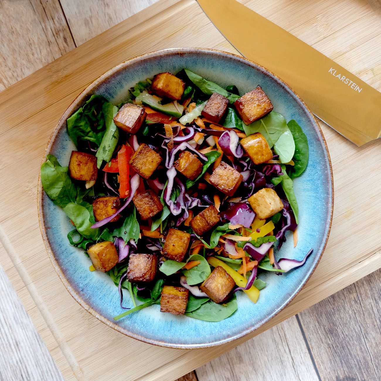 Crispy Tofu wird in einem blauen Teller auf einem Salatbett gezeigt.