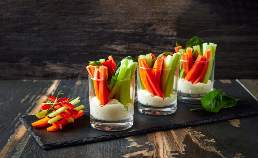 Zdravé svačiny: Zeleninové tyčinky jsou zobrazeny ve sklenici s dipem na dně.