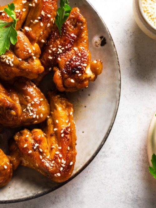 Chicken Wings aus der Heißluftfritteuse werden mit Koriander und Sesamsamen auf einem weißen Teller serviert.