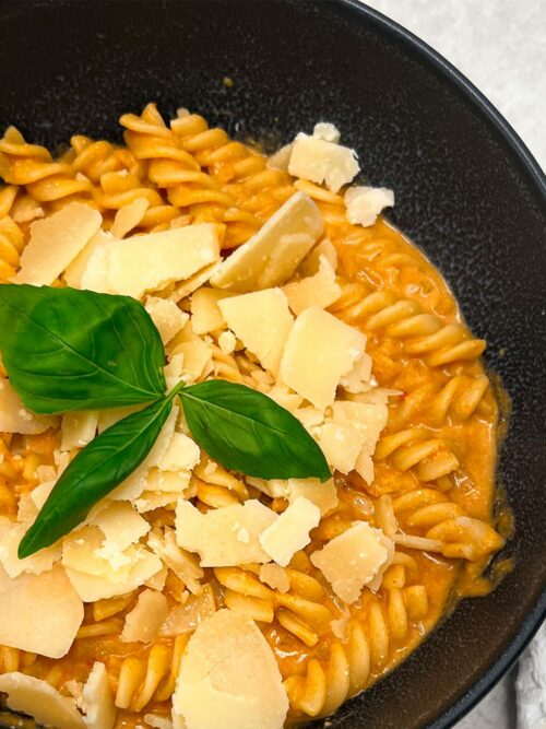 Kürbis Pasta wird in einer dunklen Schüssel mit Parmesan und Basilikum serviert.